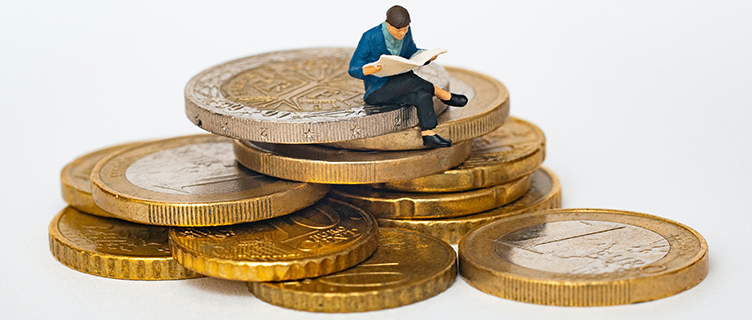 O persoană în miniatură așezată pe un morman de monede euro